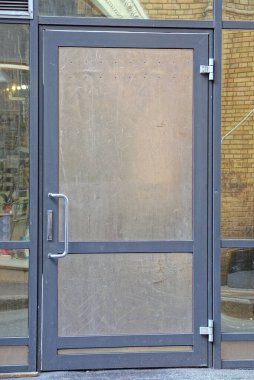 Caddedeki binanın cam duvarında gri kapalı metal bir kapı var.