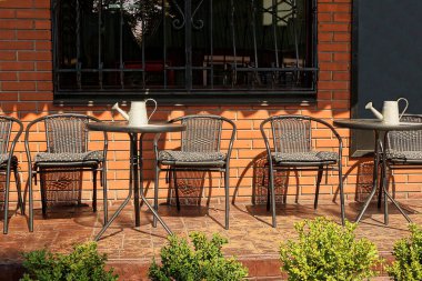 a row of black tables and chairs of a summer restaurant stand on the street against a brown brick wall with a window