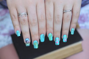 blue colored manicure on the nails of white fingers on the hands of a girl with rings