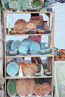 a set of colored dishes from ceramic plates with patterns stand on the wooden shelves of a showcase on the street