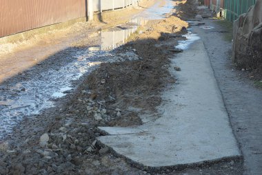 part of a road being repaired in mud and puddles with a long gray concrete broken slab on a rural street