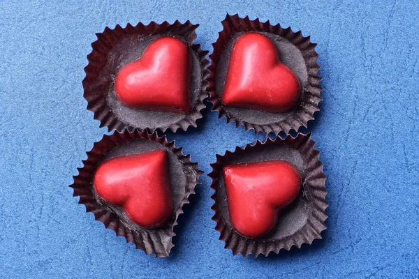 dört kırmızı kalp şekeri kahverengi kağıt paketlerde mavi bir masada.