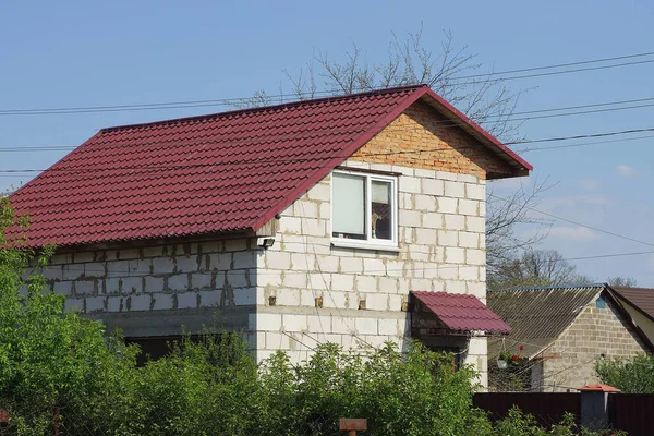 white brick  private house with a window under a red tiled roof against a blue sky in the rural street