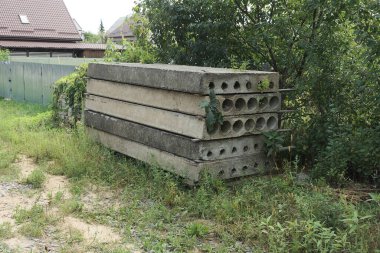 a pile of gray old concrete slabs in green grass and vegetation on a rural street