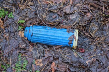 one old dirty plastic blue thermos lies on wet fallen brown leaves in nature
