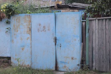 blue old closed metal gate in brown rust on a gray wooden fence wall in a rural street
