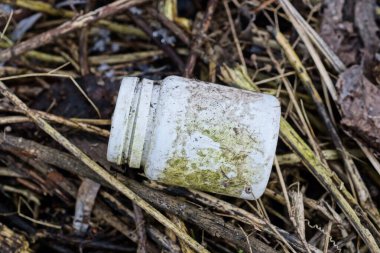 garbage from one small dirty white plastic bottle lies on brown branches of plants on the street