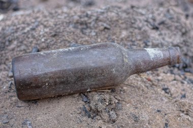 garbage from one dirty old glass brown bottle lies on the gray ground on the street