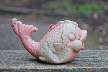 one old plastic red white toy fish stands on a gray wooden table in the street