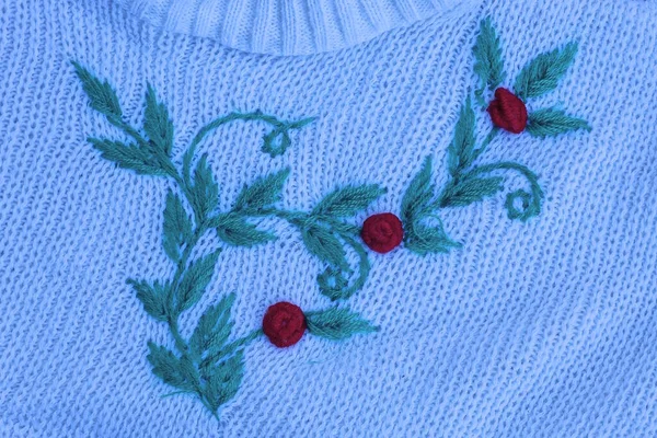 colored embroidery in the form of a green branch with leaves and red berries on white woolen fabric on clothes