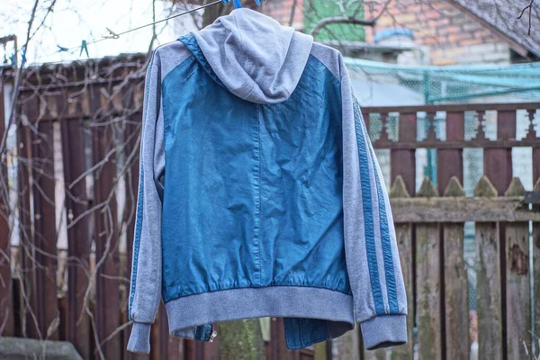 one hooded jacket made of blue leather and gray fabric hangs on a wire in the street