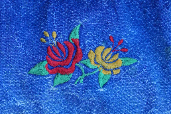 embroidery with colored threads in the form of two flowers on a blue cotton fabric on clothes