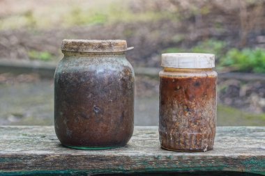 İki kirli cam kavanoz ve kırmızı reçel sokakta gri bir masada duruyor.