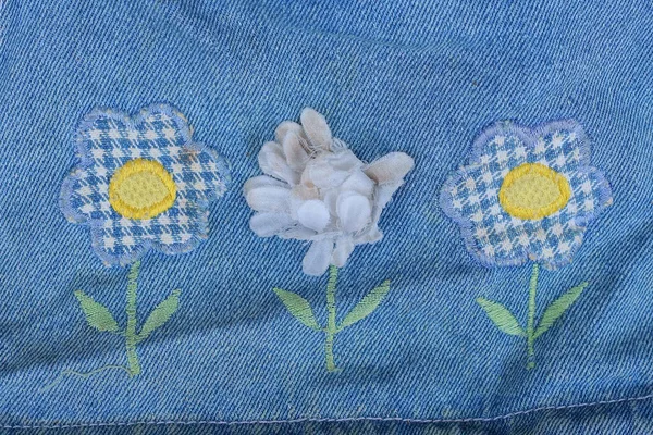 embroidery with colored threads in the form of three flowers on a blue cotton fabric on clothes