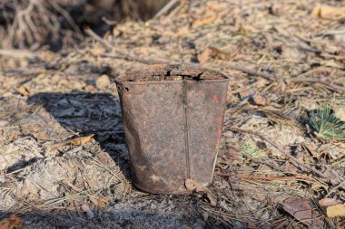 Büyük, kahverengi, paslı bir teneke kutu gri kuru yaprakların üzerinde duruyor.