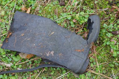 Siyah, eski, yırtık bir lastik bot doğadaki yeşil bitki örtüsünde yatıyor.