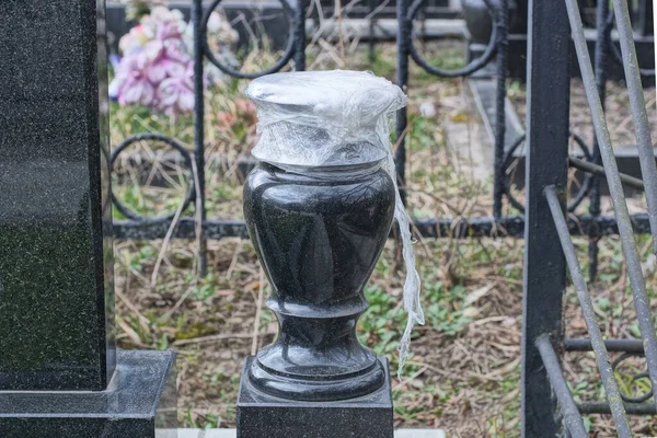 白いセロファンで覆われた黒い石の花瓶が墓地の大理石の記念碑の近くの墓の上に立っている — ストック写真