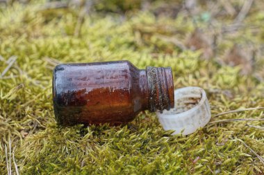 Doğada yeşil yosunların üzerinde beyaz kapaklı küçük, açık kahverengi bir tıbbi şişe var.