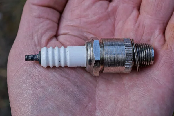 one small metal white gray spark plug lies on the open palm of the hand