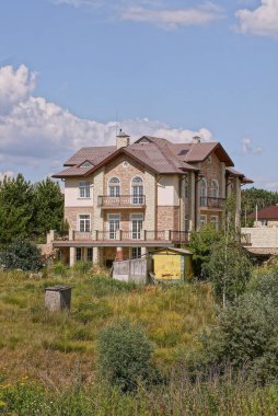 Kahverengi kiremitli çatının altında yeşil çimlerde ve bitkilerde mavi gökyüzüne karşı büyük gri bir ev.