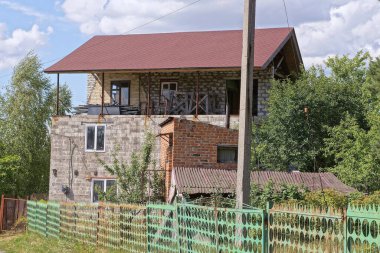 büyük gri tuğlalı özel bir ev kahverengi kiremitli bir çatı altında yeşil bitki örtüsünün arasında metal bir çitin arkasında