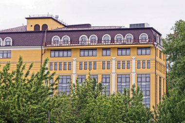 Gri gökyüzüne karşı yeşil ağaçların arasında büyük kahverengi bir gökdelen.