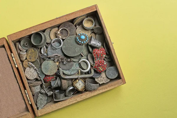 a pile of old coins of jewelry and ornaments in a wooden box on a yellow table