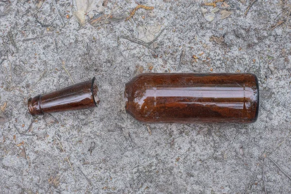one brown glass bottle broken into two parts lies on the gray sand on the street