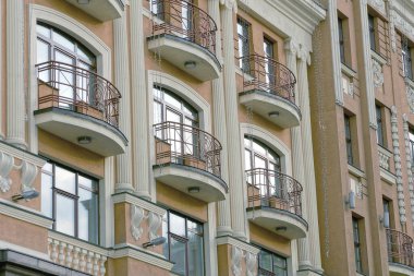 Şehir sokaklarında cam pencereli ve kapısı olan büyük bir evin taş duvarında bir sıra açık kahverengi demir balkon.
