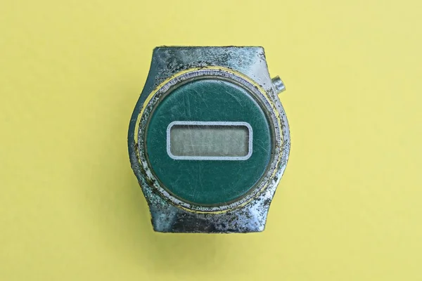 one old shabby gray green electronic wrist watch lies on a yellow table