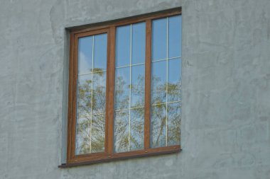 Caddedeki evin gri beton duvarında büyük kahverengi bir pencere var.