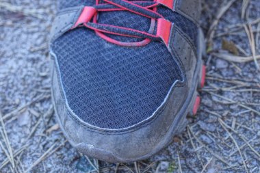Deri ve kumaştan yapılmış siyah kırmızı bir spor ayakkabının parçası Gri bir zeminde duruyor