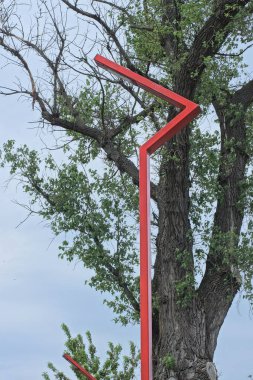 Yüksek kırmızı metal kıvrımlı bir direk. Sokakta, ağaçların ve gökyüzünün arka planında fener lambaları var.