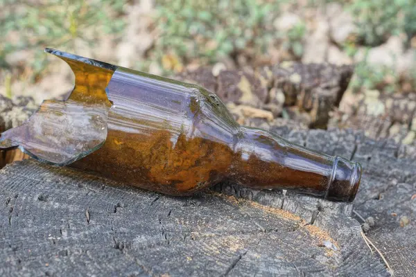 one brown broken glass bottle lies on a gray wooden stump on the street