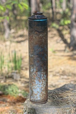 Uzun, paslı, yanmış metal bir teneke kutu doğada bir kütüğün üzerinde duruyor.