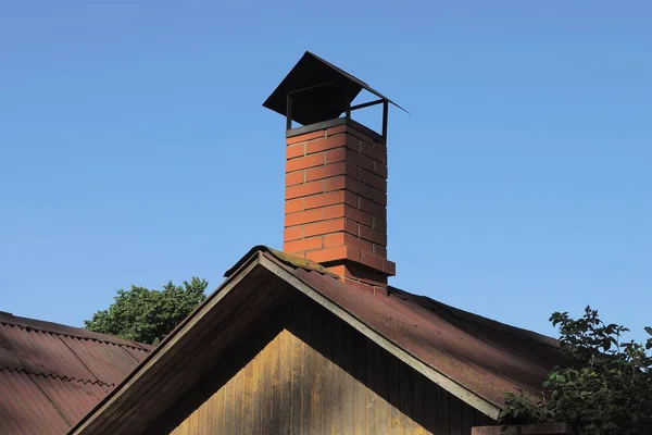 青い空に対して屋外の田舎の家の灰色の木製のロフトのスレート屋根の上の1つの茶色のレンガの煙突 — ストック写真