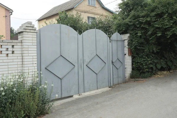 沥青路面附近街道上绿色植被篱笆白色砖墙上的一个灰色金属门和一个铁门 — 图库照片