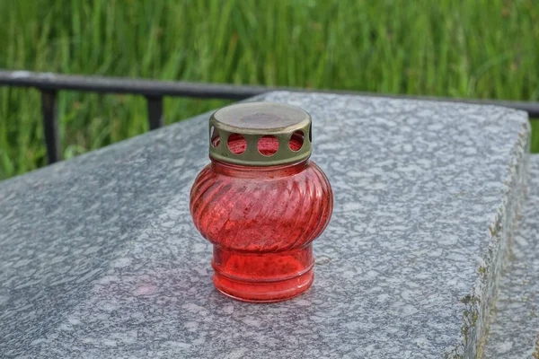 one red glass candle lamp with a brown metal lid stands on a gray marble tombstone on a grave in a cemetery