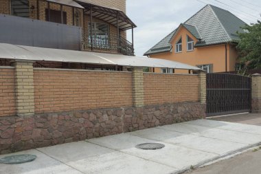Kapalı demir kapılı bir çitin uzun kahverengi tuğlalı duvarı caddedeki büyük özel bir evin önünde.