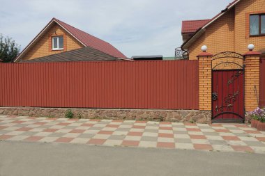 Uzun kırmızı bir çit duvarı ve kaldırımdaki kırsal bir sokakta siyah işlemeli demir deseni olan demir bir kapı.