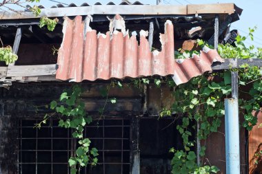 Eski, yanmış, terk edilmiş bir evin parçası. Çatısı kırmızı kırılan bir levha parçası. Gökyüzüne karşı.