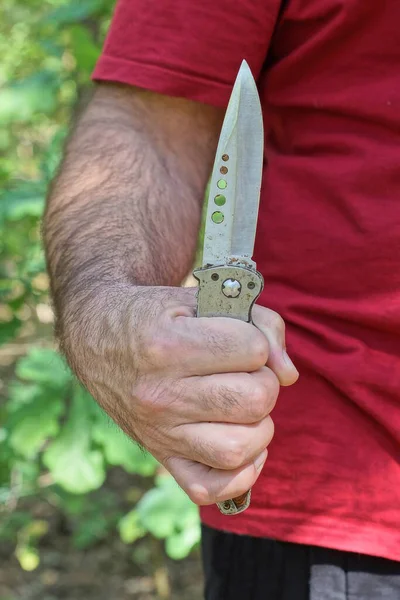 赤い服の男の手には自然の中で屋外に大きな折り畳み式の狩猟ナイフがある — ストック写真
