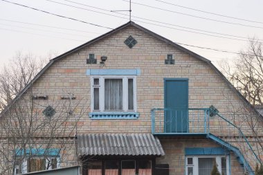 Açık yeşil metal bir balkon, kahverengi tuğlalı bir tavan arasında merdiven. Kapısı ve kırsal bir sokakta gri gökyüzüne bakan bir pencere var.