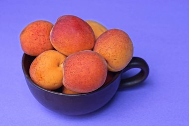 Olgun meyveli bir yemek kahverengi bir fincanda kırmızı kayısılar bir leylak masasında duruyor.