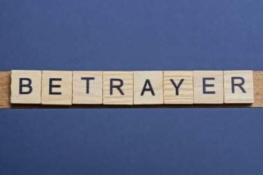 İhanet kelimesini kahverengi ahşap küçük harflerle siyah bir masanın üzerine yaz.