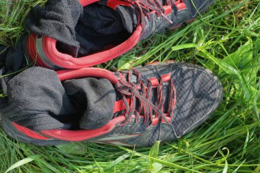 Çoraplı iki siyah kırmızı spor ayakkabı doğada yeşil çimlerde duruyor.