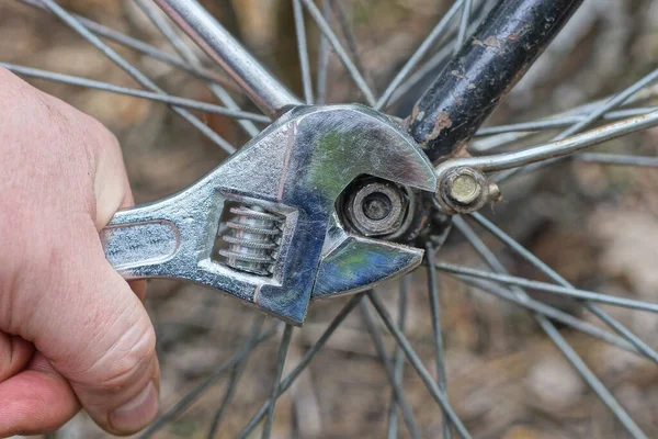 灰色の調節可能なレンチを持つ手は黒いフレームと自転車の車輪の上にナットを締めます — ストック写真