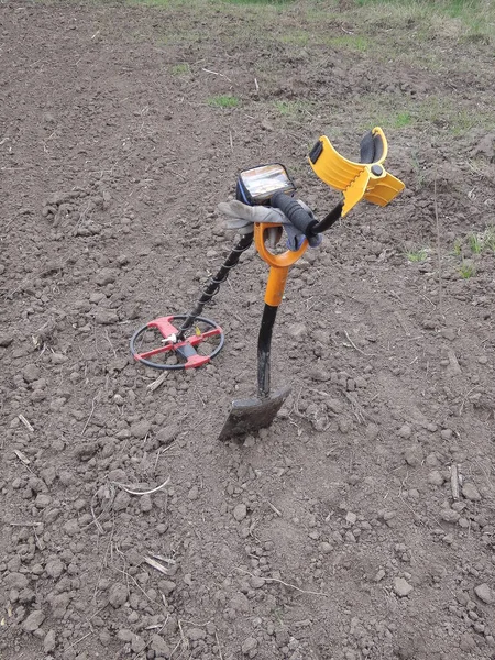 one yellow metal detector on a black steel shovel stand on gray ground in a field in nature