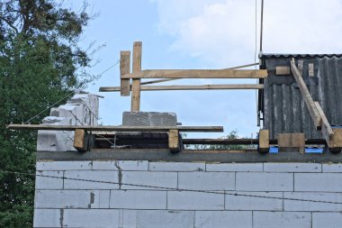 Tamamlanmamış beyaz tuğlalı bir evin parçası. Çatısında tahtalar ve mavi gökyüzüne karşı ahşap kahverengi şekiller var.