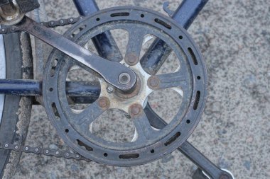Üzerinde yıldız işareti olan siyah metal bir pedal ve eski bir bisikletin demir iskeletinde bir zincir sokaktaki gri asfaltta yatıyor.